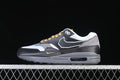 Side view of black, grey, and white Nike Air Max 1 sneakers with gold-tone laces and a visible Air midsole unit