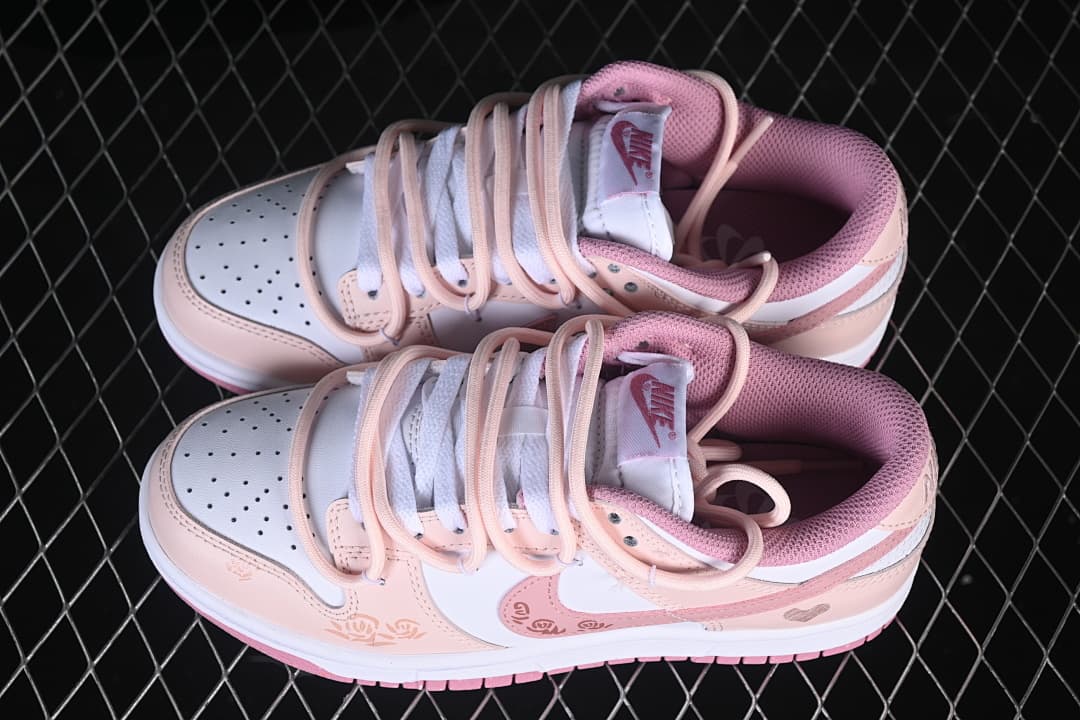 Pair of white and pink Nike SB Dunk Low sneakers with layered strap-style lacing and floral details