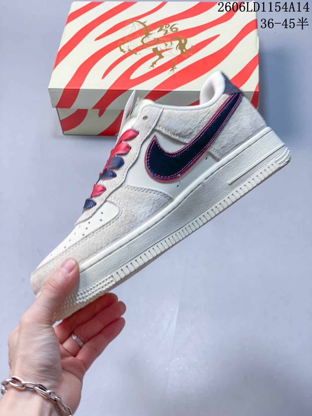 Side view of a cream Nike Air Force 1 '07 sneaker with a navy Swoosh edged in red