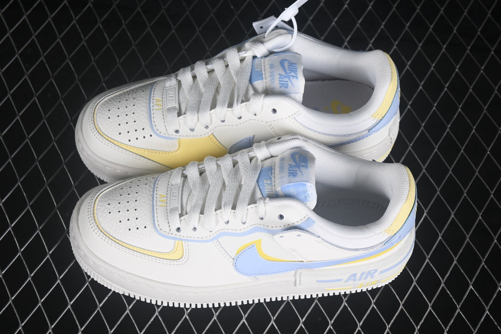 Angled overhead view of the pair showing the white uppers, light blue and yellow overlays, laces, and layered soles.
