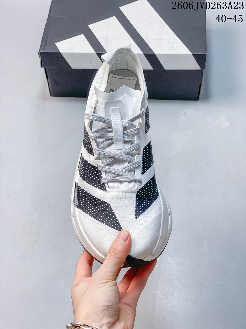 Top view of a white Adidas lace-up shoe with dark three-stripe detailing; image overlay states sizes 40–45.