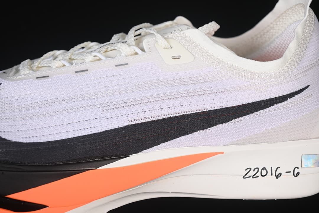 Close-up of the white upper, black side graphic, and orange midsole detail.