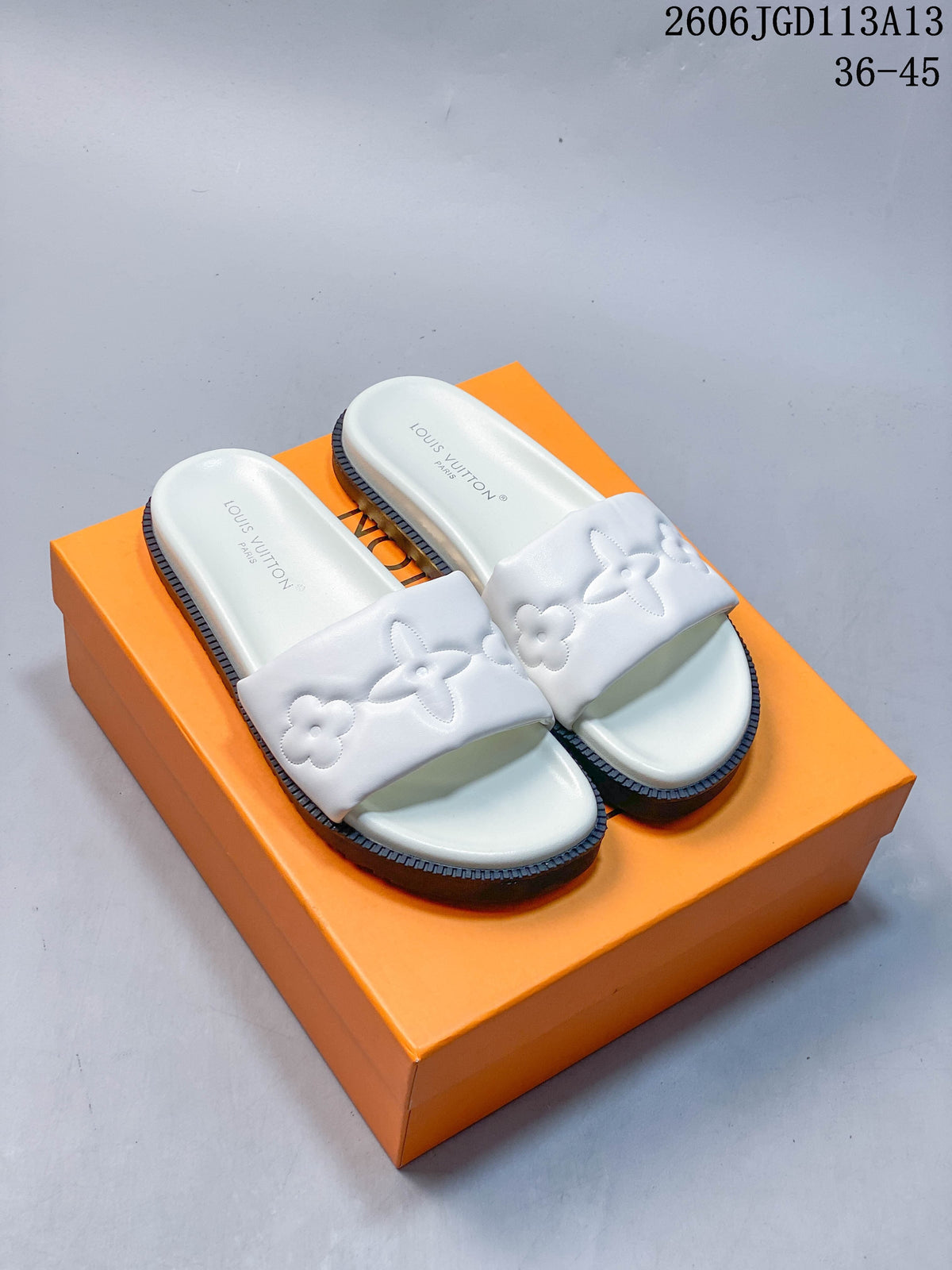 White slide sandals with raised floral motifs and a thick dark ridged outsole, photographed on an orange box.
