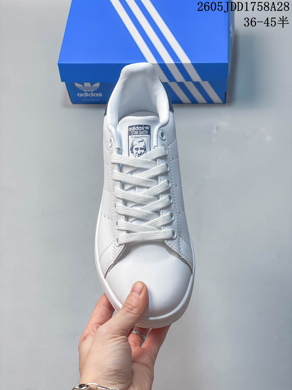 Front view of a white lace-up sneaker with a portrait graphic on the tongue label.