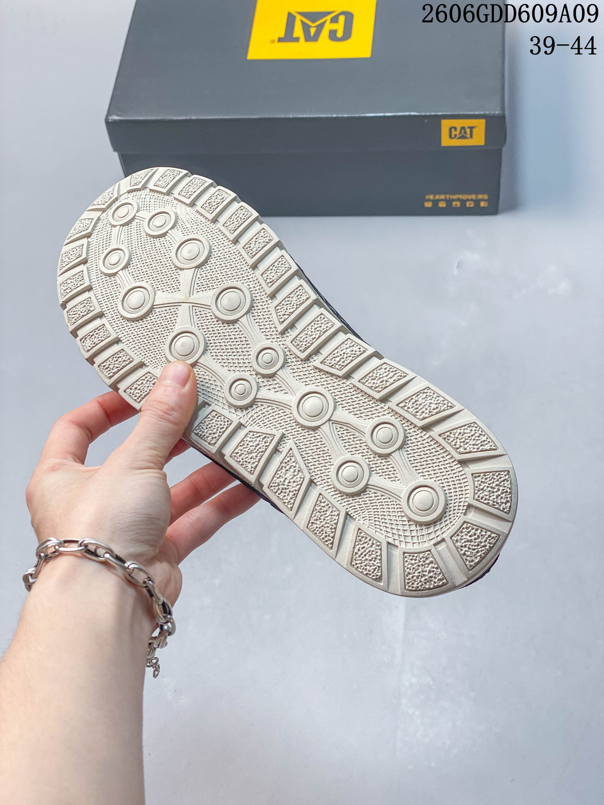 Textured light-colored outsole of a navy sandal, with CAT shoe box in the background; image overlay shows sizes 39–44.
