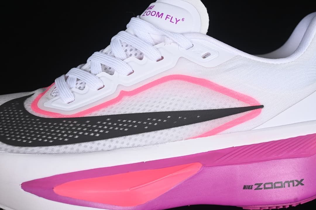 Close-up of white laces, tongue branding, black Swoosh, and pink accents