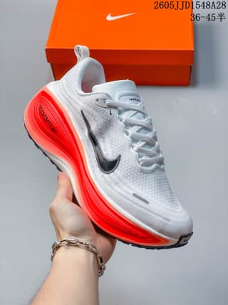 White Nike Vomero Plus shoe with a black swoosh and bright red midsole accents.
