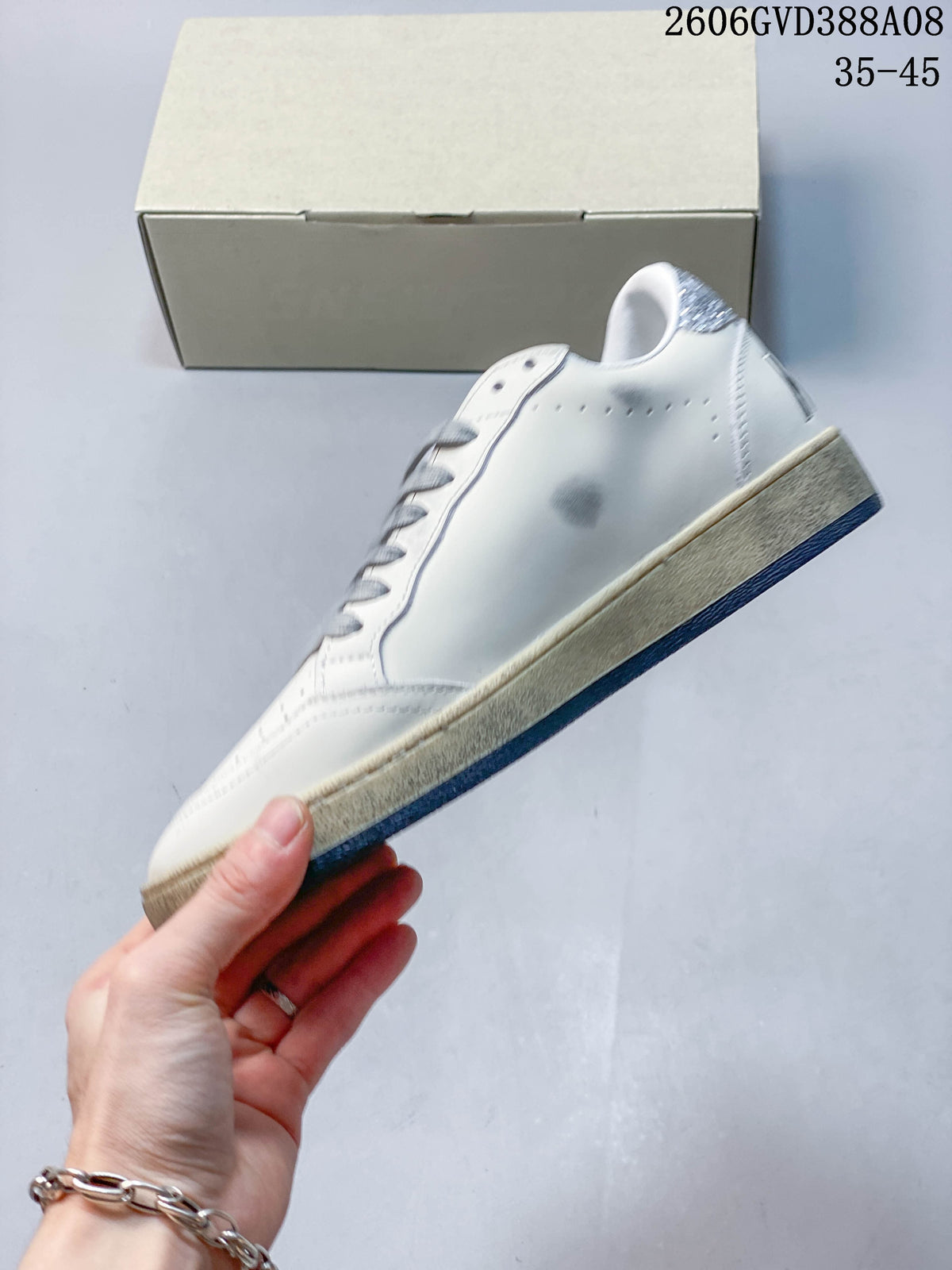 Side view of white sneaker with perforations, silver glitter heel tab, and beige midsole