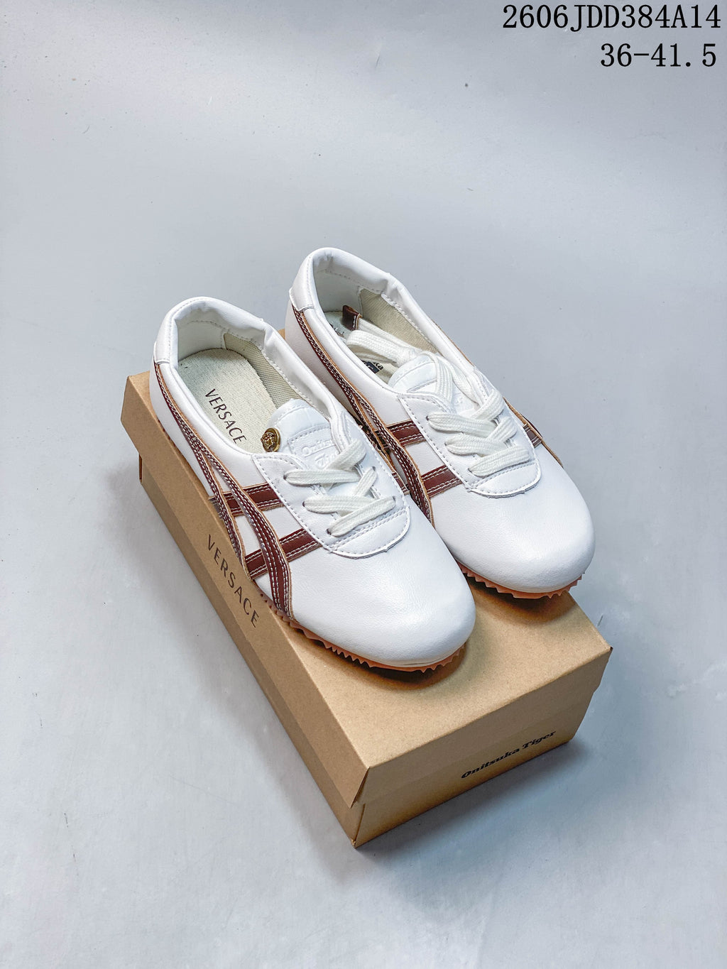 White low-top lace-up sneakers with brown side stripes, shown on a shoe box