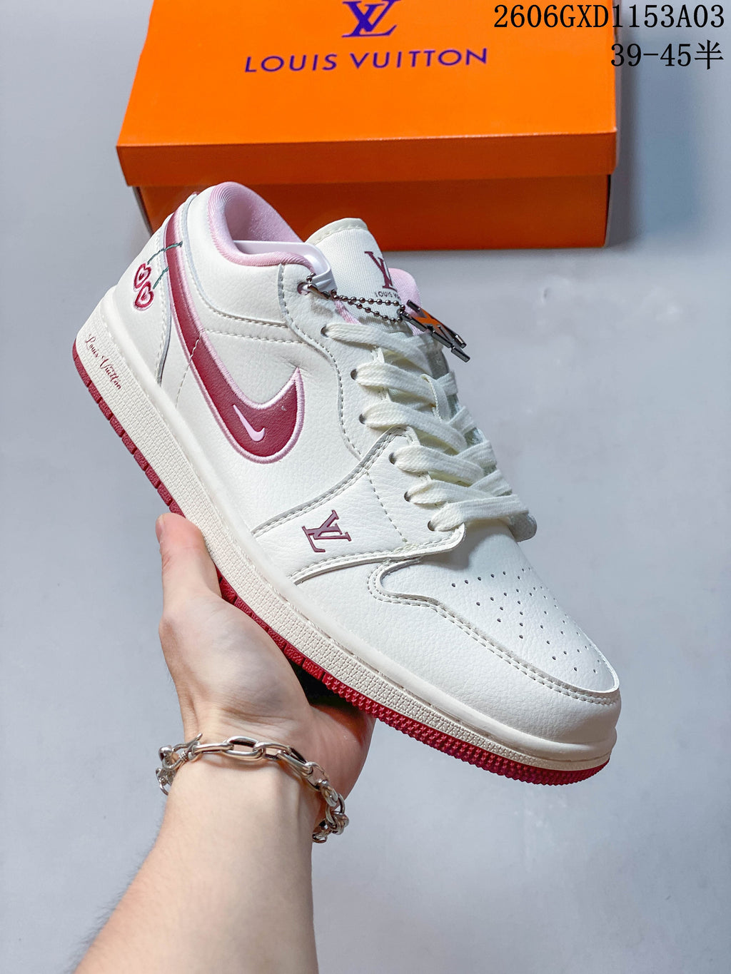 Angled side view of a white and pink low-top sneaker with a decorative lace charm.