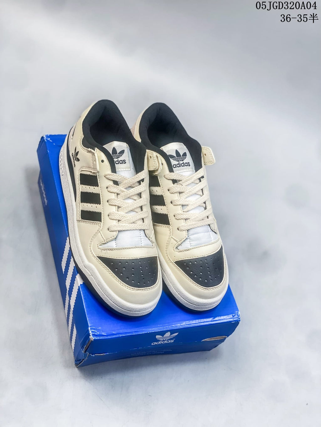 Pair of cream and black Adidas Forum 84 Low sneakers shown from above on a blue shoe box.
