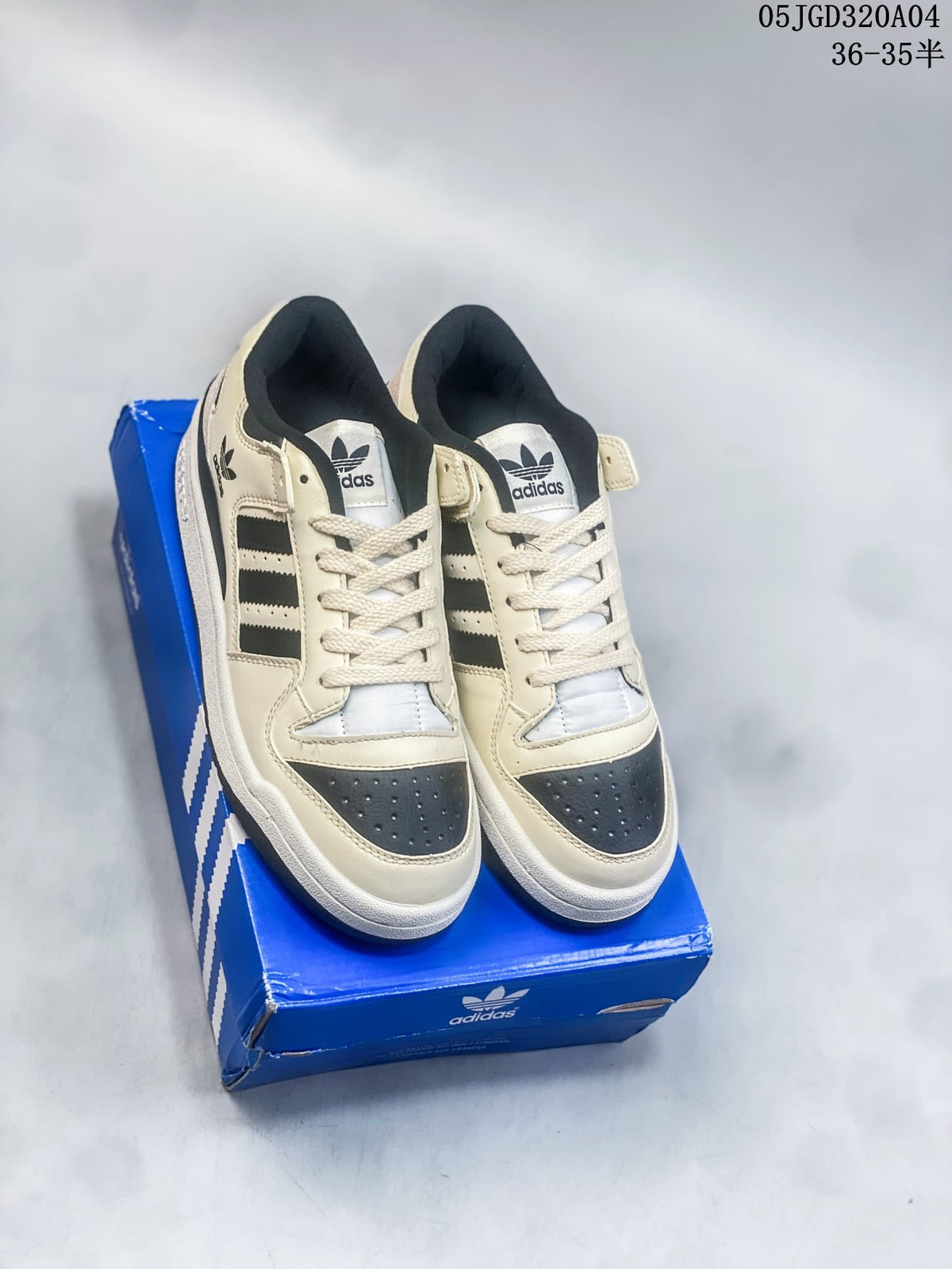 Pair of cream and black Adidas Forum 84 Low sneakers shown from above on a blue shoe box.
