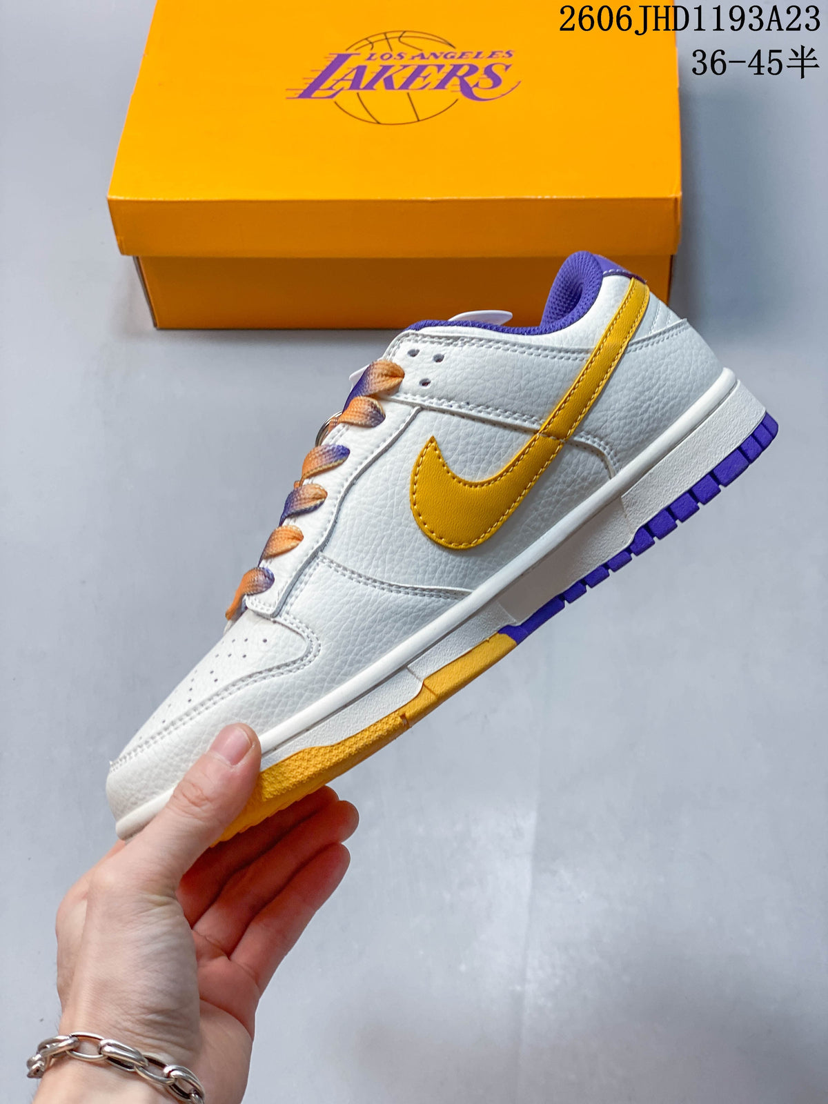 Side profile of a white low-top sneaker with gold Swoosh, purple outsole accents, and Lakers-branded box