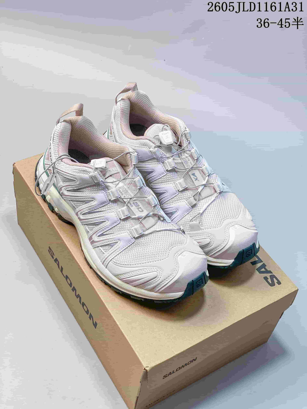 Pair of white Salomon XA Pro 3D sneakers with lilac and teal accents on a shoe box