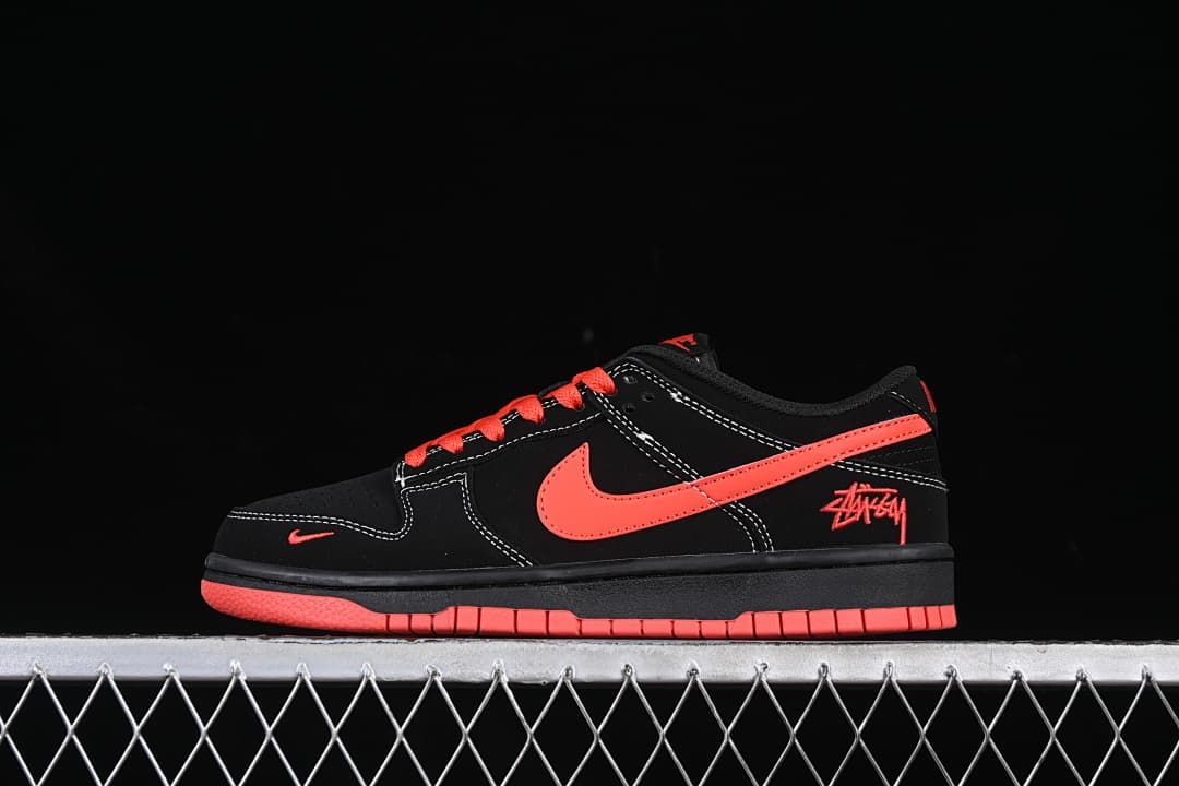 Side profile of a black low-top sneaker with red-orange accents and script detail at the heel.