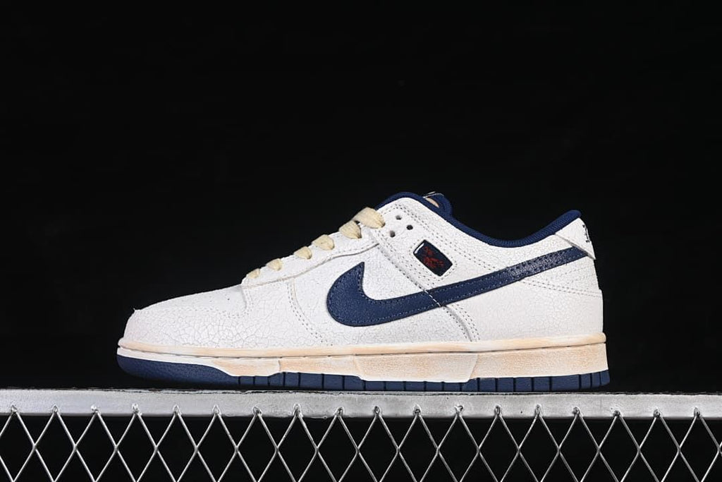 Side view of off-white and navy Nike SB Dunk Low sneakers with cream laces
