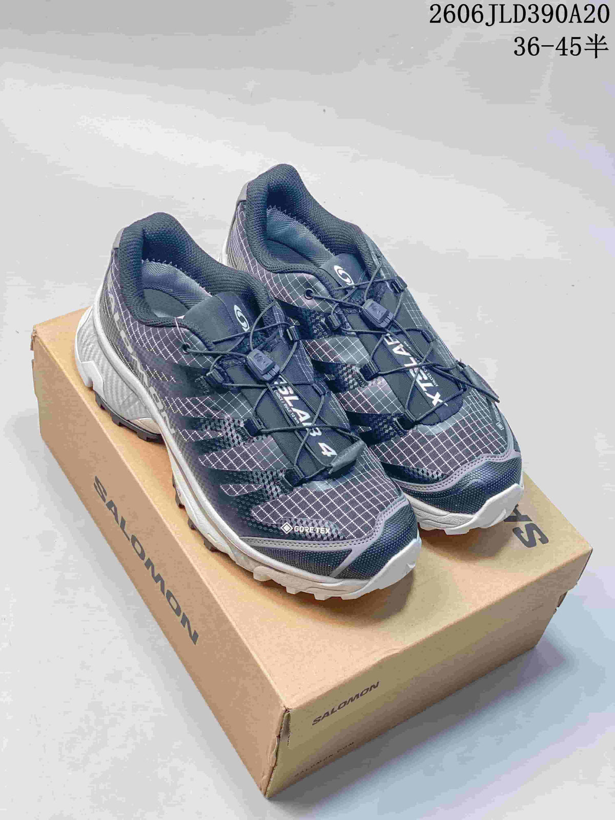 Pair of dark gray and navy patterned Salomon XT-4 OG shoes on a box; image overlay shows a size range.
