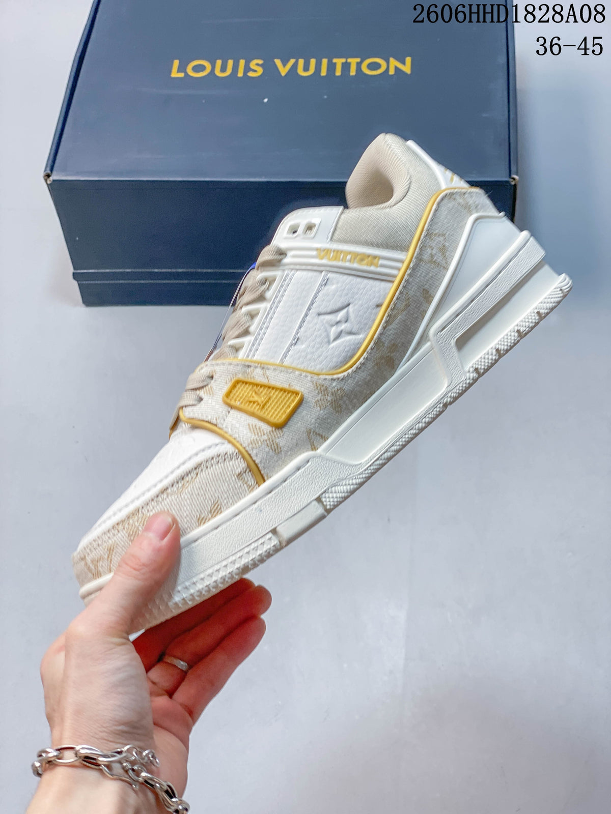 Side view of a white and beige low-top sneaker with patterned trim and gold-tone accents.