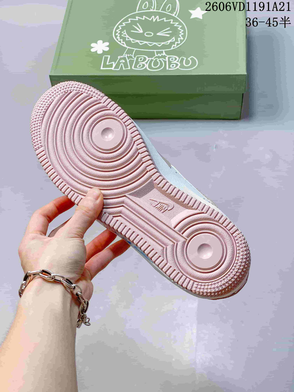 Pink outsole of the sneaker held in front of a green Labubu-branded box