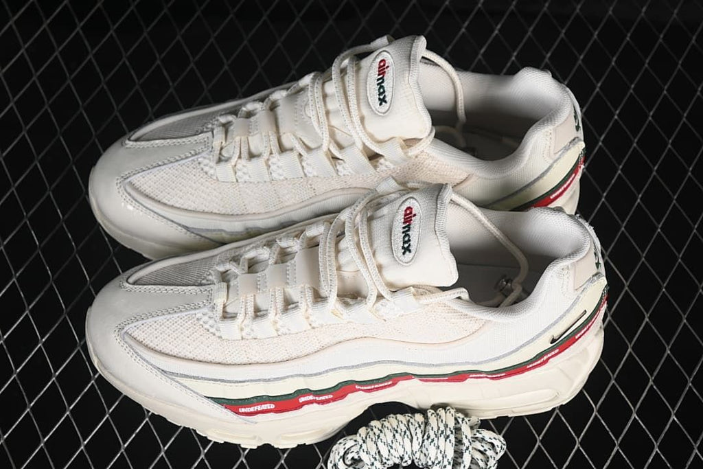 Pair of off-white sneakers with green and red side stripes and spare patterned laces.