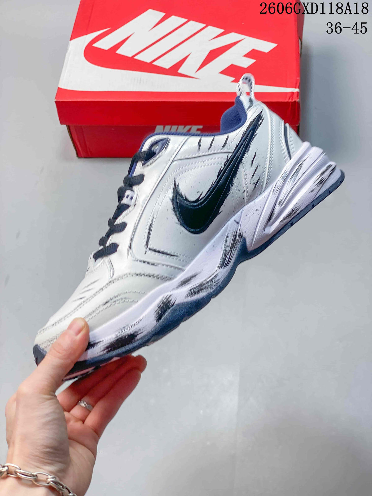 Side profile of a white Nike Air Monarch sneaker with a dark Swoosh and graphic upper detailing.