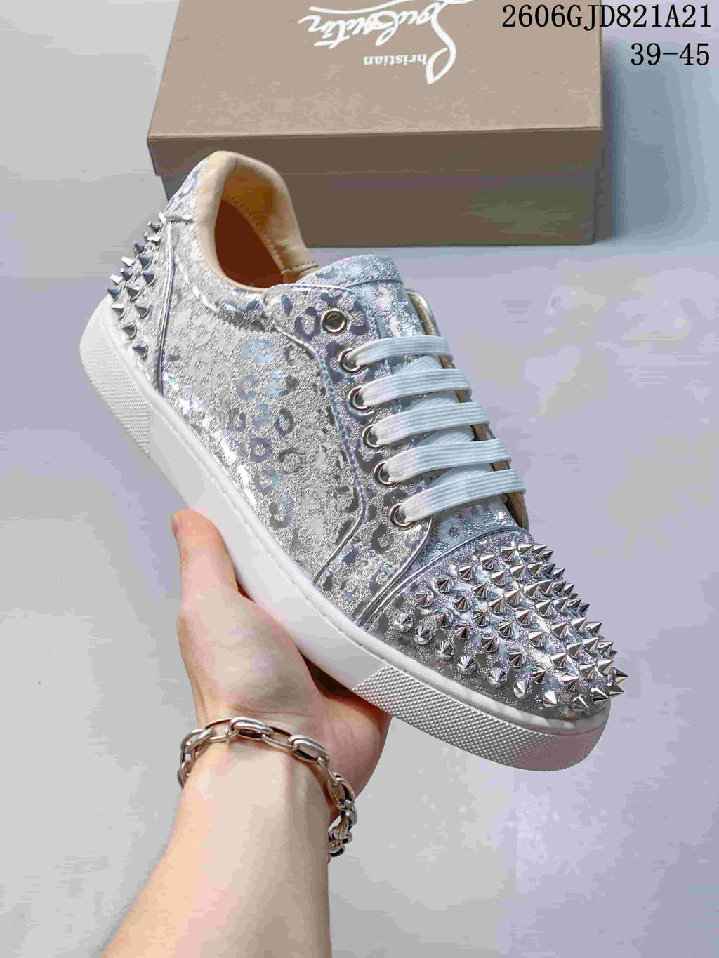Angled view of a silver patterned sneaker with white laces and metallic studs