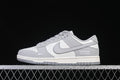 Side view of gray and white Nike SB Dunk Low sneakers on a metal fence.