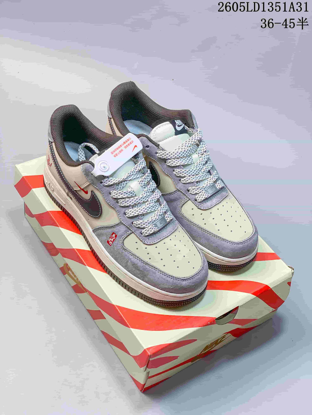 Pair of off-white and gray Nike Air Force 1 Low sneakers on a red-and-cream striped box