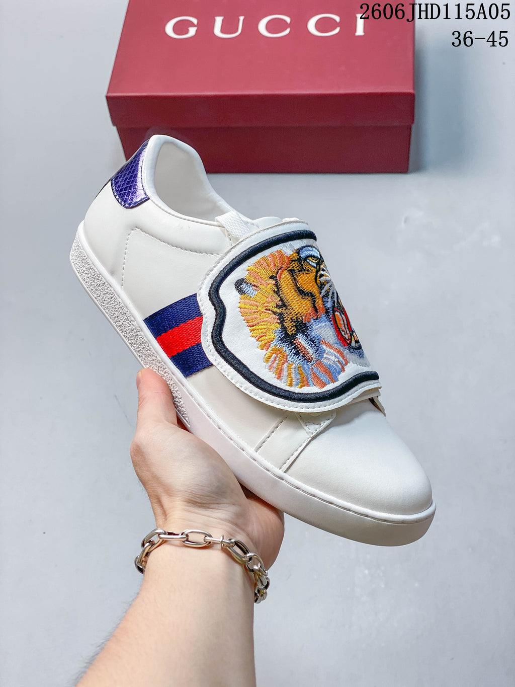 White low-top sneaker with an embroidered tiger-face tongue flap and red-and-blue side stripe.
