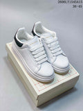 Pair of white low-top sneakers with navy heel tabs and chunky white soles, shown on a box.