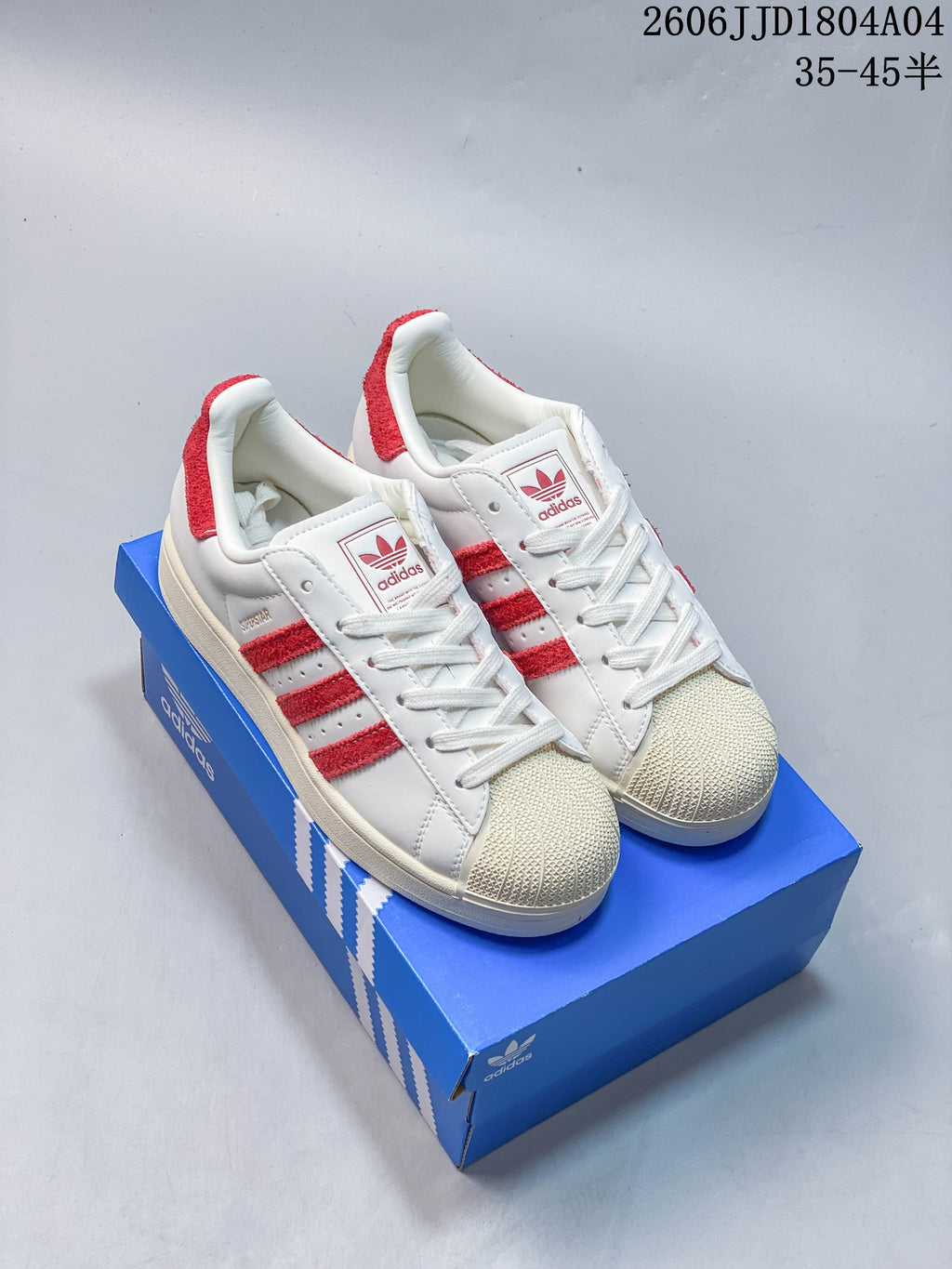 Pair of white sneakers with red side stripes and shell-style toes on a blue shoebox.