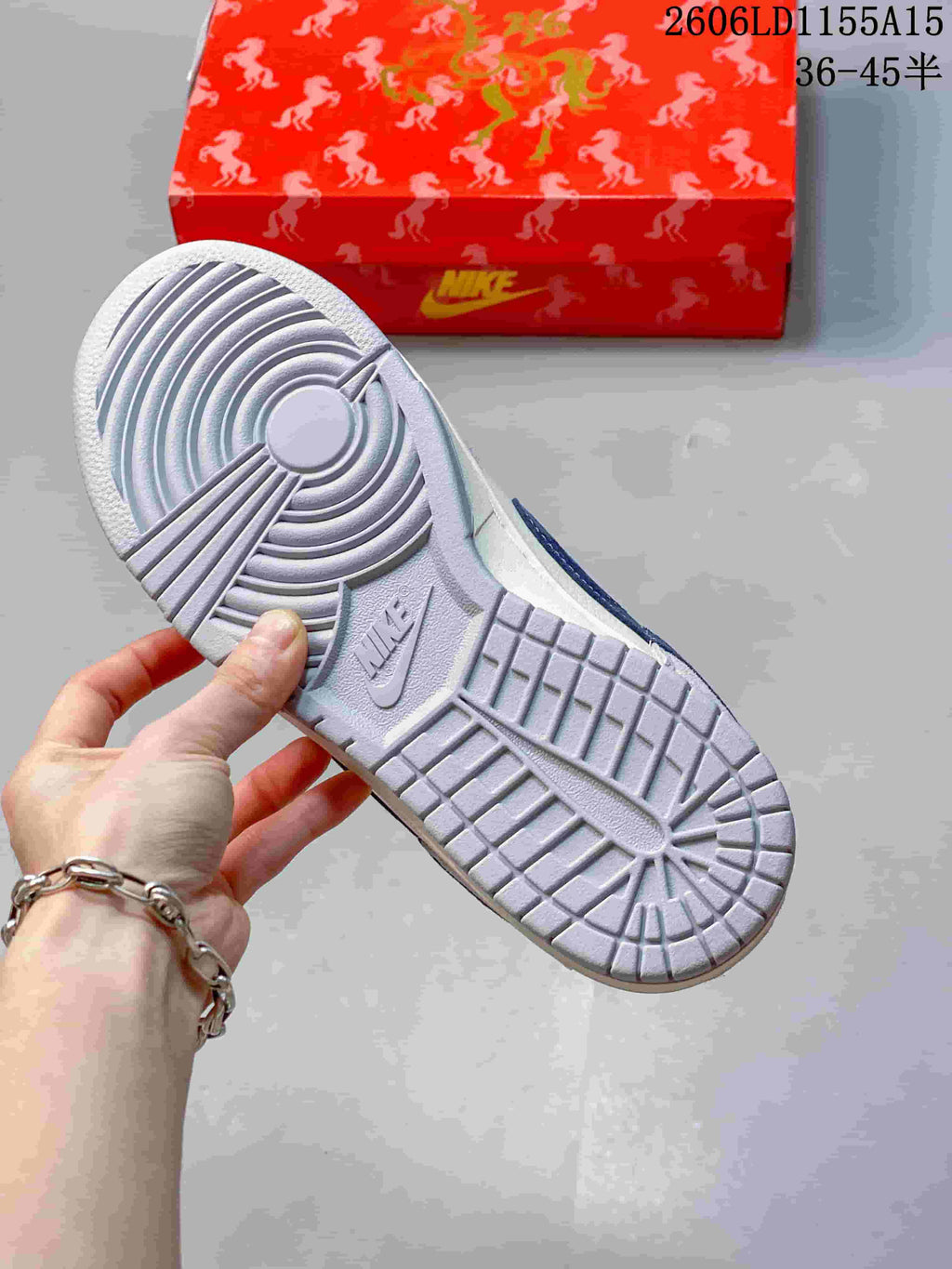Outsole view of the grey Nike SB Dunk Low beside a patterned red box