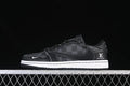 Side view of a black low-top sneaker with charcoal check-pattern panels, contrast stitching, a white midsole, and visible swoosh and monogram-style branding.