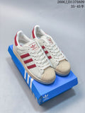 Pair of cream adidas Superstar sneakers with red accents, shell toes and a blue shoe box.