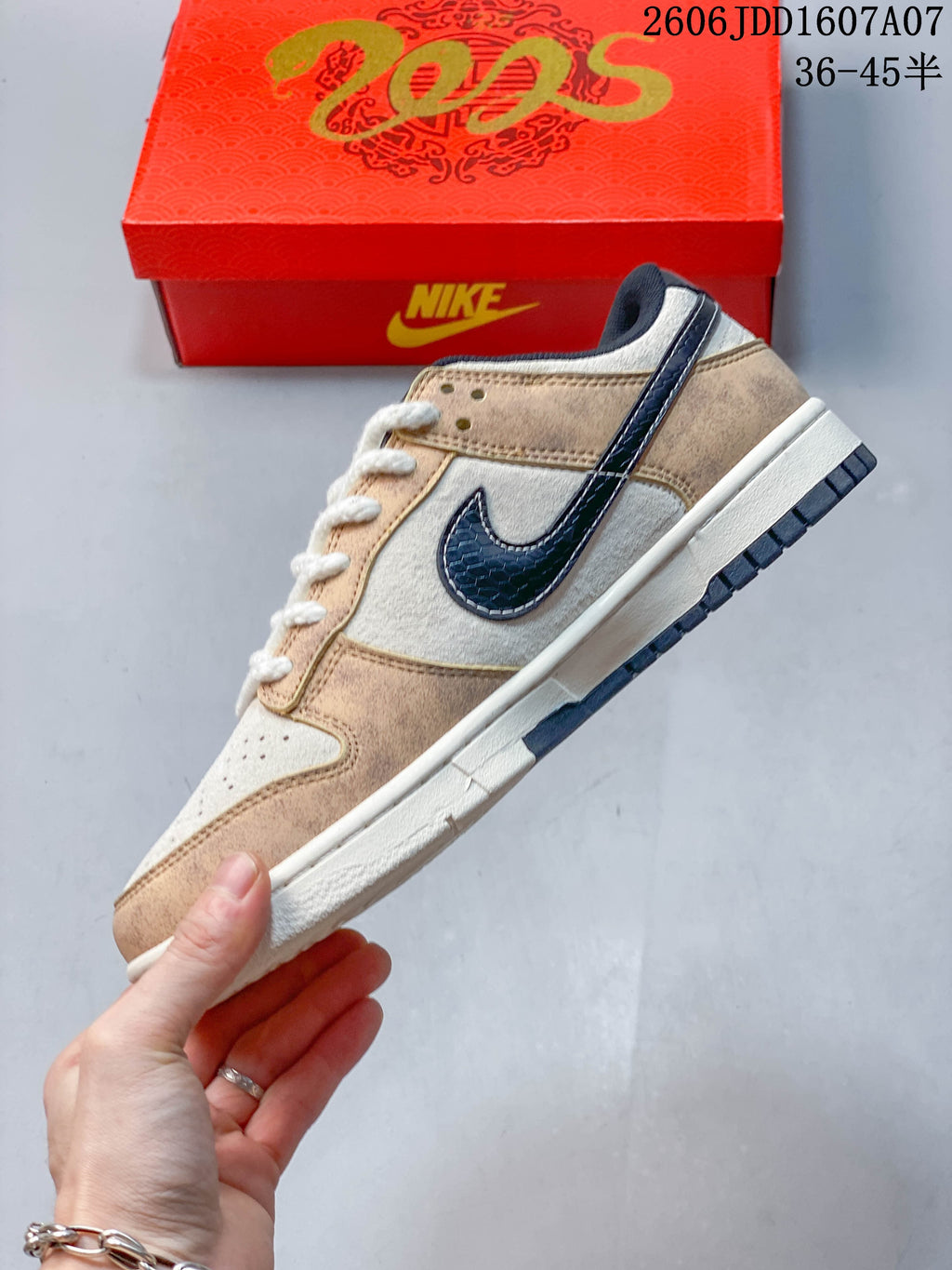 Side profile of a beige and cream Nike SB Dunk Low with a dark navy Swoosh; image overlay states sizes 36–45.5.