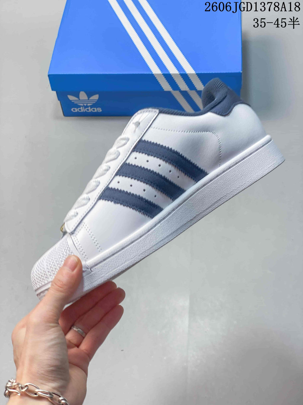 Side view of a white Adidas Superstar sneaker with navy stripes and shell-style toe.