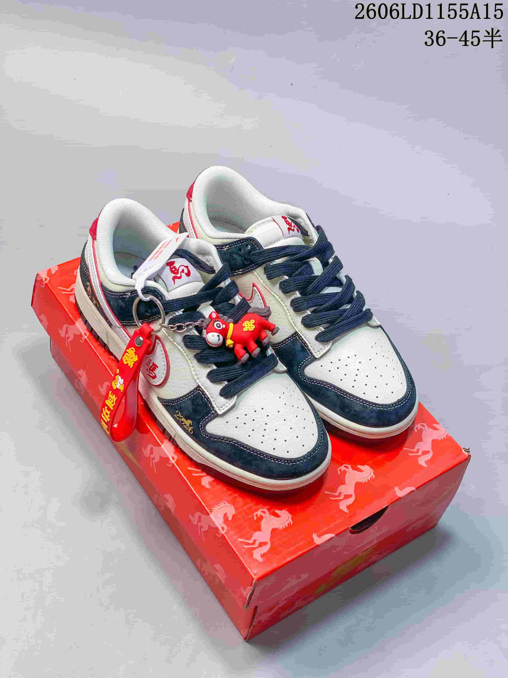 Pair of off-white and navy Nike SB Dunk Low style sneakers with red accents, charms and a red patterned box