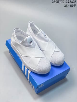 White Adidas Superstar-style slip-on shoes with crossed straps on a blue shoe box.