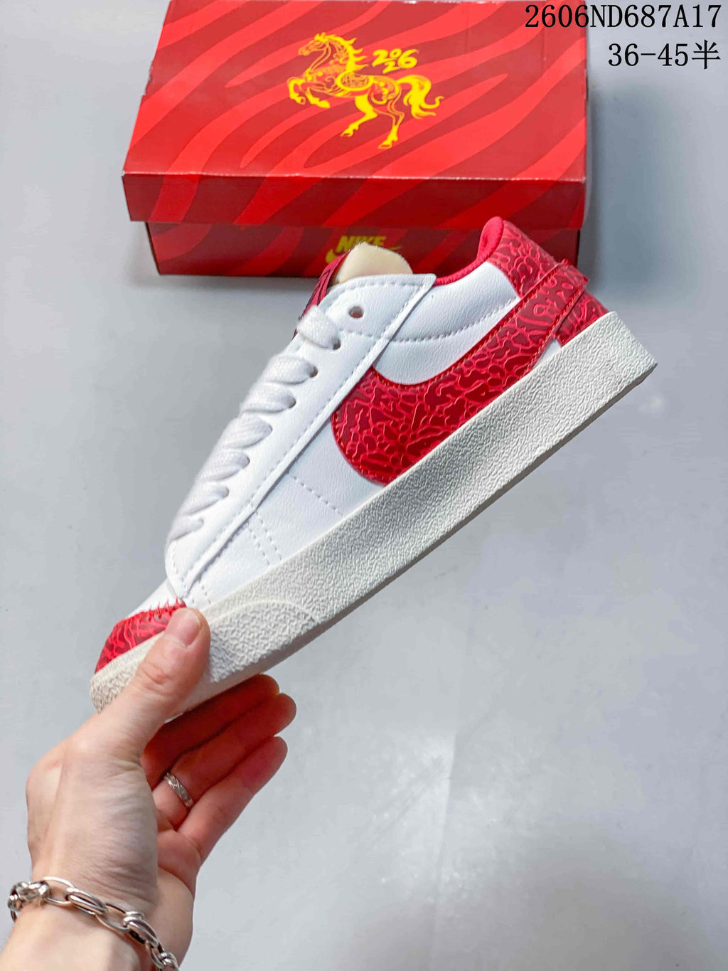 Side view of a white sneaker with red patterned Swoosh and heel accents.