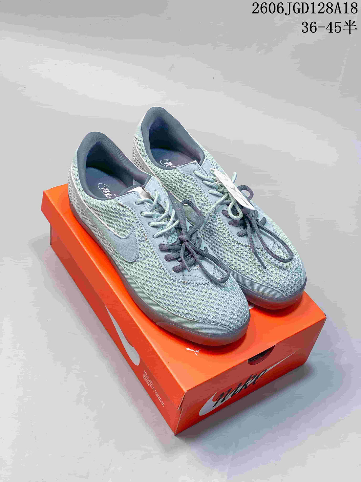 Pair of gray-green Nike Astrograbber low-top sneakers with mesh-style panels and contrasting laces, photographed on an orange shoebox.