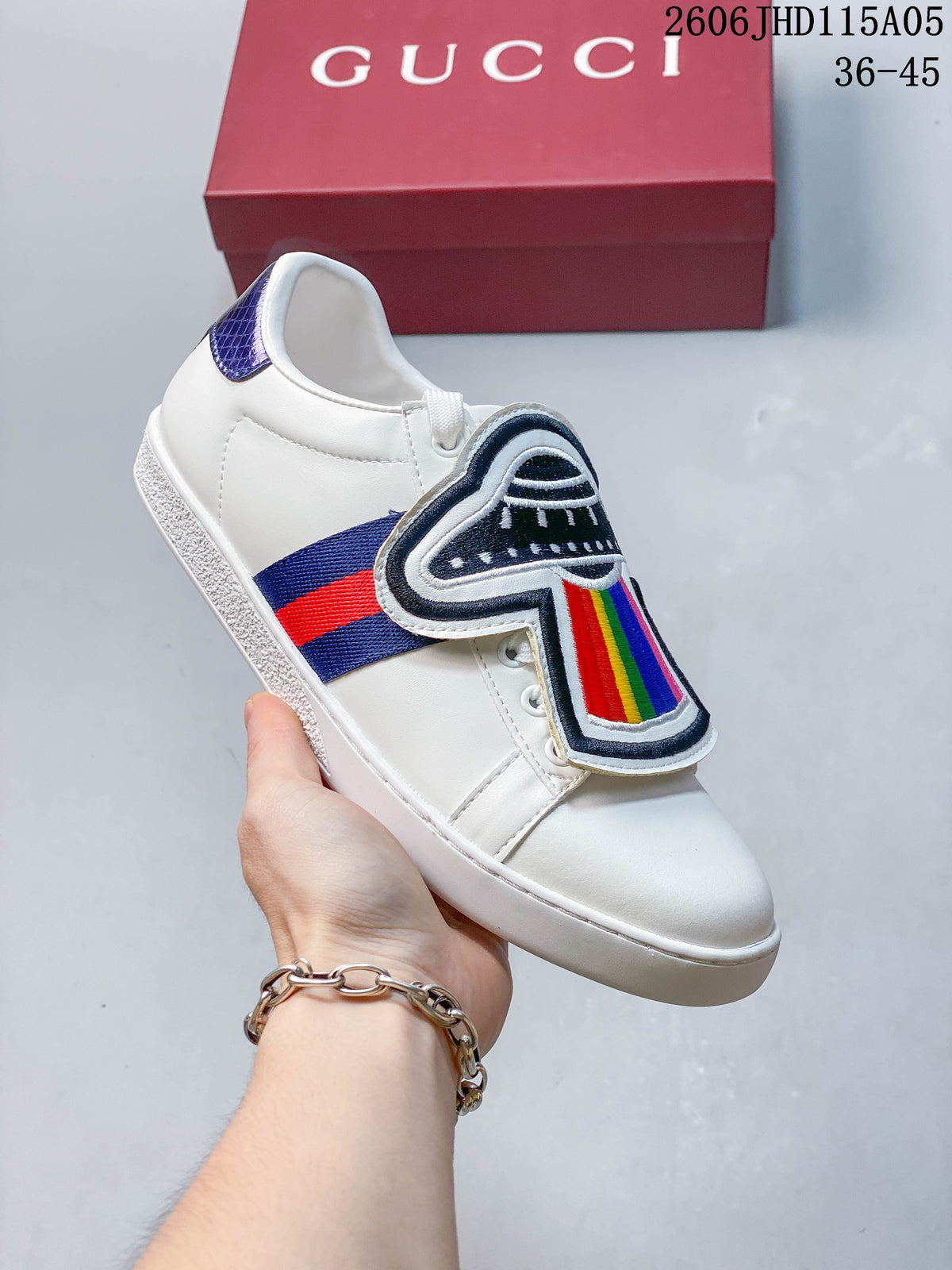 White low-top sneaker with a dark embroidered graphic and rainbow detail on the tongue flap.