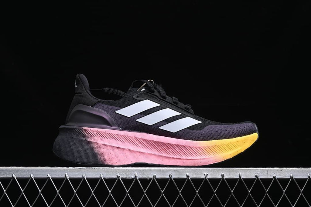 Side profile of the shoe with white stripes and a pink-to-yellow midsole.