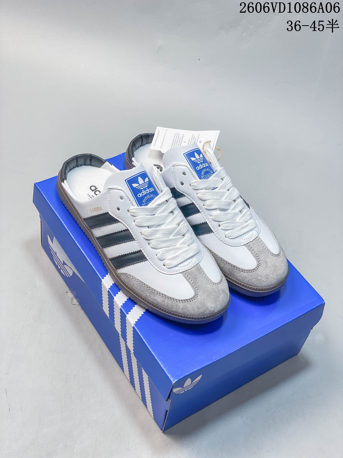 White and gray Adidas Samba-style low-top sneakers with dark stripes, shown on a blue box.