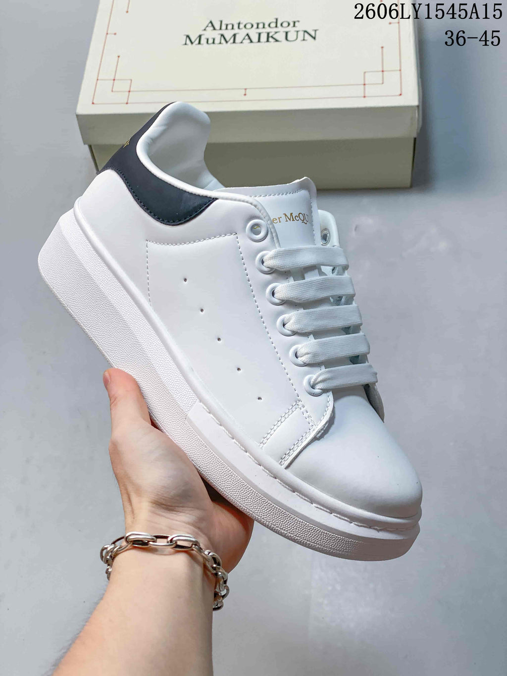 Side view of a white sneaker with a dark grey heel panel and contrasting white sole.