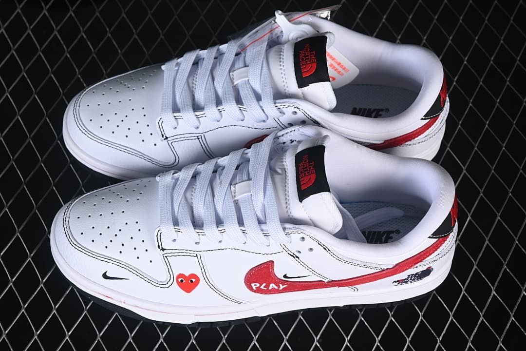 Pair of white low-top sneakers shown from above, with white laces, perforated toe panels, red side graphics and black accents.