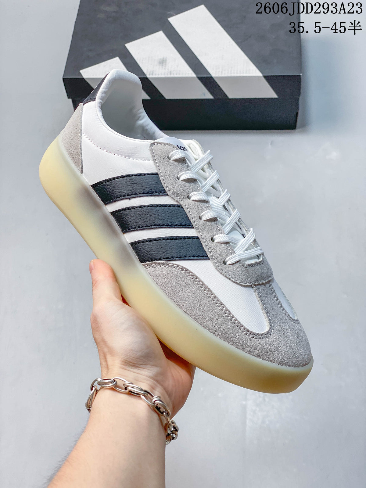 Close-up of a white and gray Adidas Barreda Decode sneaker with dark stripes and a translucent-looking sole.
