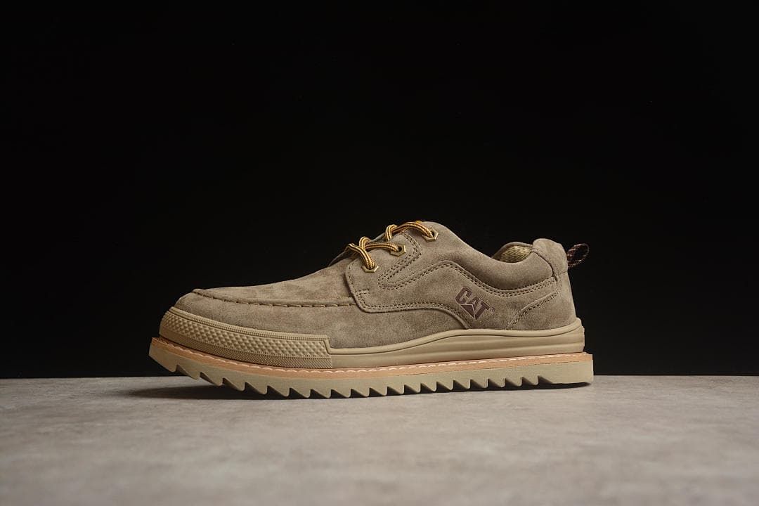 Side view of a taupe-brown CAT shoe against a dark background