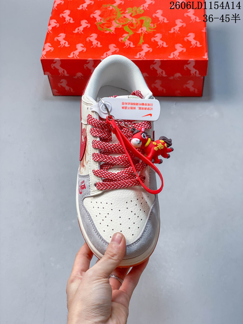 Top view of an off-white low-top sneaker with red-and-white laces, perforated toe, grey overlays, and decorative charms.