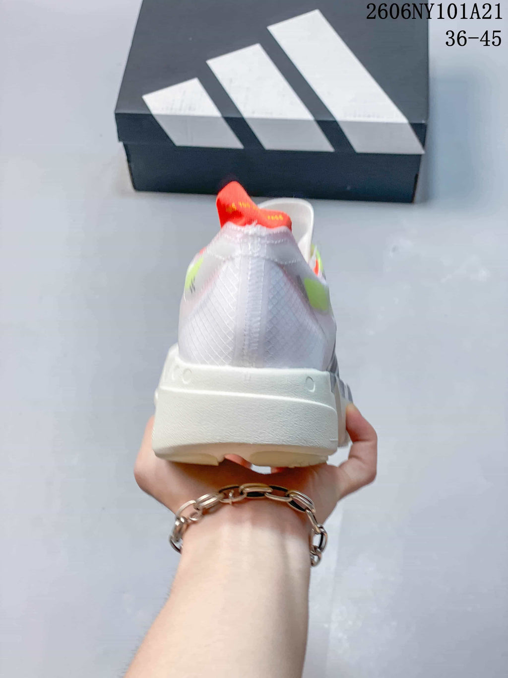 Rear view of a white Adidas shoe with orange-red heel detail and sculpted off-white sole.