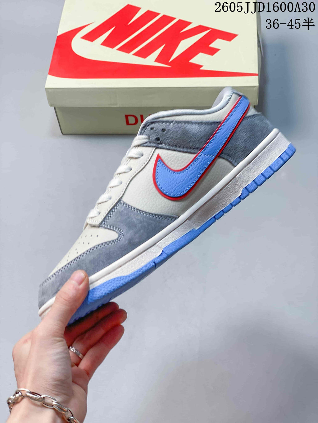 Side view of a light grey Nike SB Dunk Low sneaker with blue Swoosh and red outline